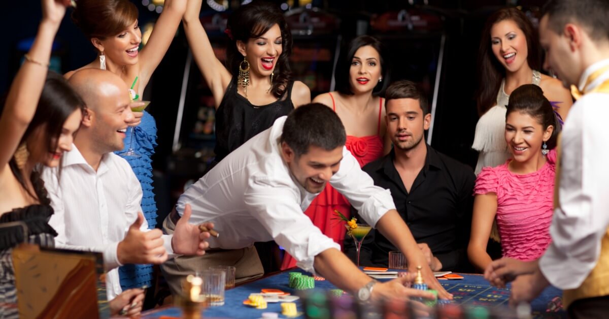 Complete Casino Rental Packages Explained A group of people gathered around a roulette table. One man is reaching into the middle to gather up chips.