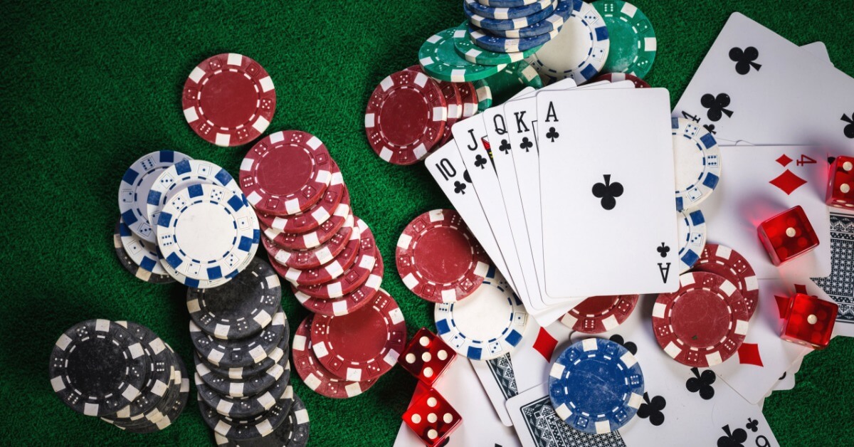 A collection of multicolored poker chips and a stack of playing cards fanned out on top of a green casino table.