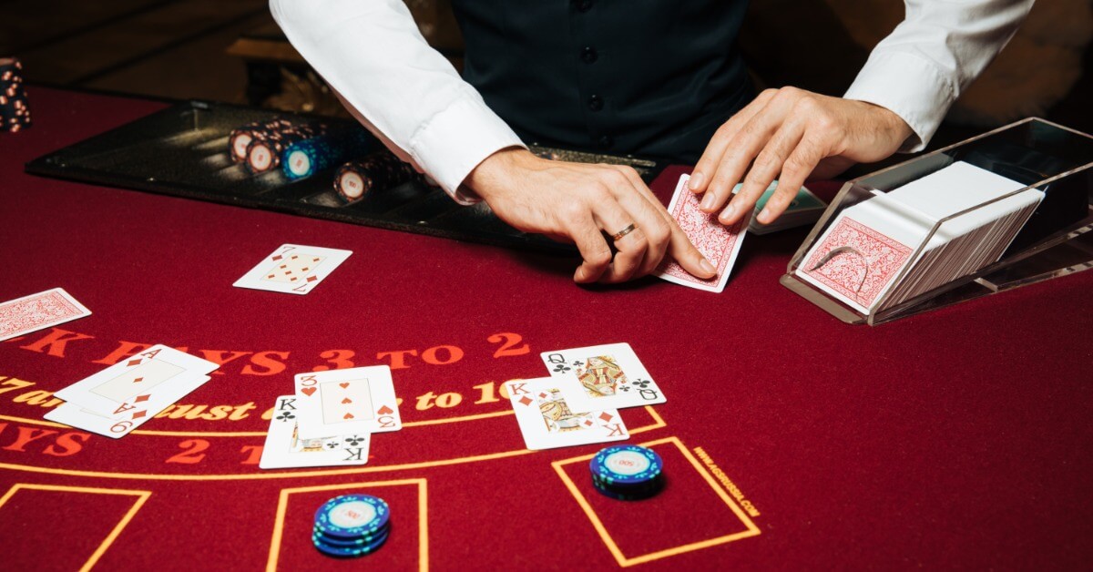 Dos and Don’ts of Blackjack Party Rentals A blackjack dealer who is about to flip over one of his cards standing in front of a table with other cards face up on it.