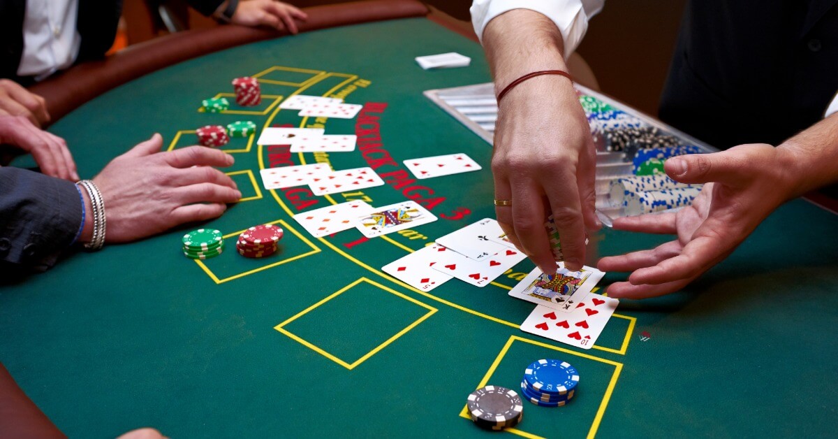 A closeup on a blackjack table with multiple people standing around the cards. A dealer is dealing out more cards.