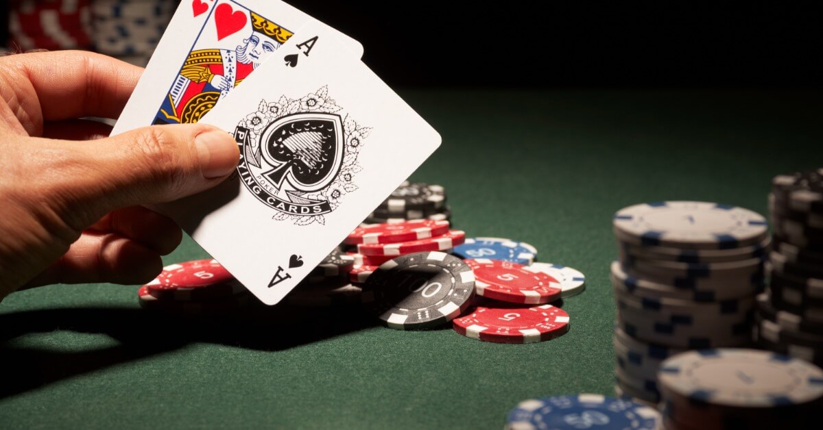A hand holding a pair of playing cards, a king and an ace. The hand is positioned in front of stacks of poker chips.