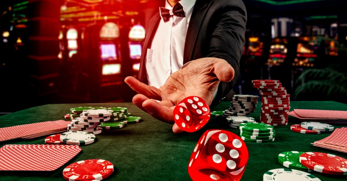 Different Types of Corporate Casino Games A man in a suit throwing a pair of red dice onto a table that is covered with poker chips and playing cards.