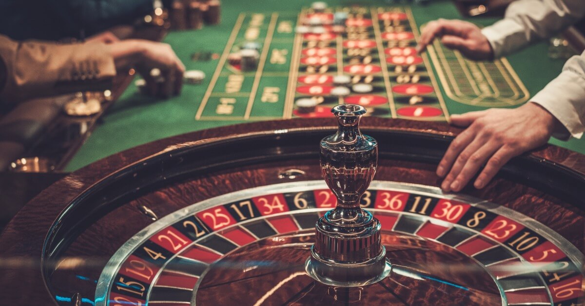 A very fancy looking roulette wheel on a casino table. There are multiple people’s hands placing bets on the table. A very fancy looking roulette wheel on a casino table. There are multiple people's hands placing bets on the table.