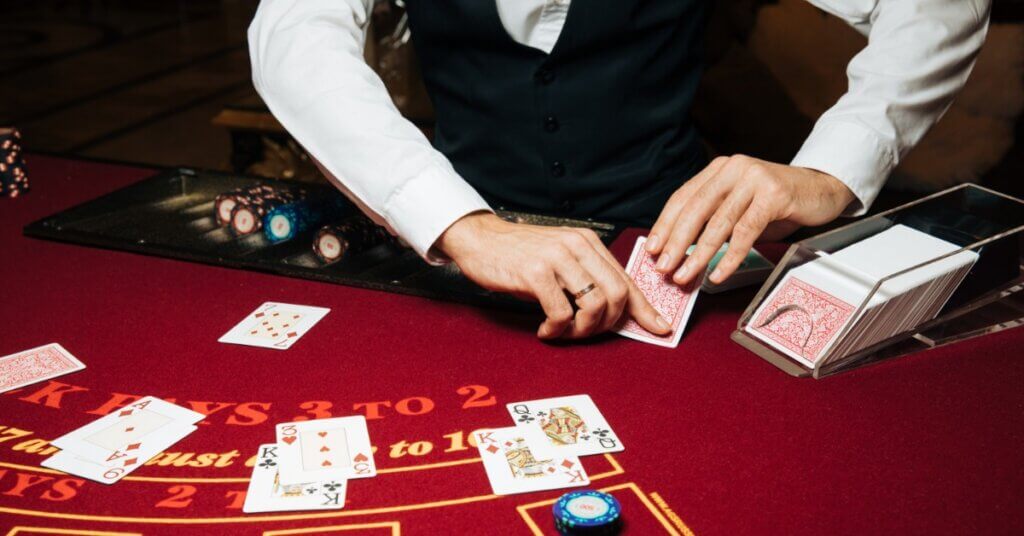 A blackjack dealer dealing out cards to four different places on the table. A few poker chips are on the table as bets.