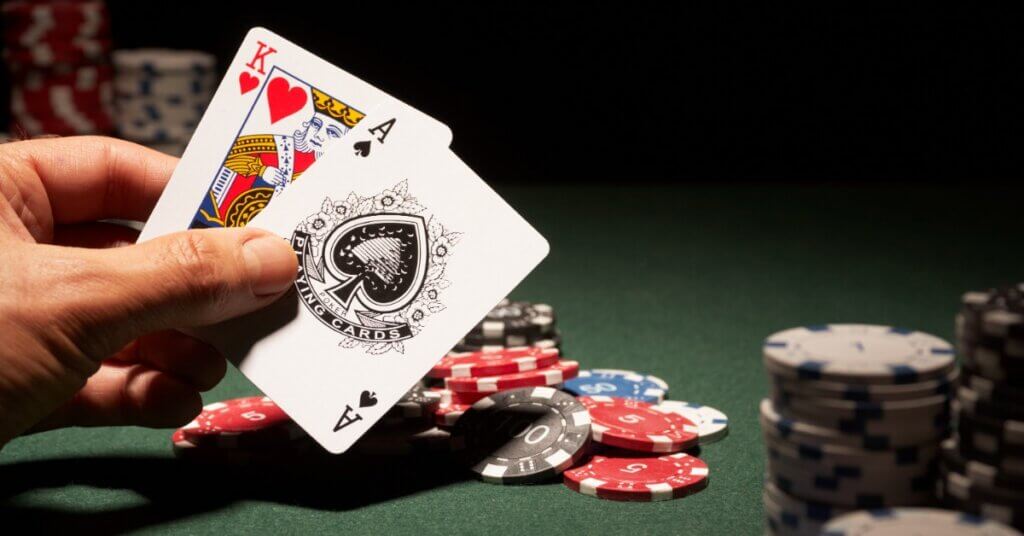 A hand holding two playing cards, a king and an ace. There are poker chips scattered around the table.